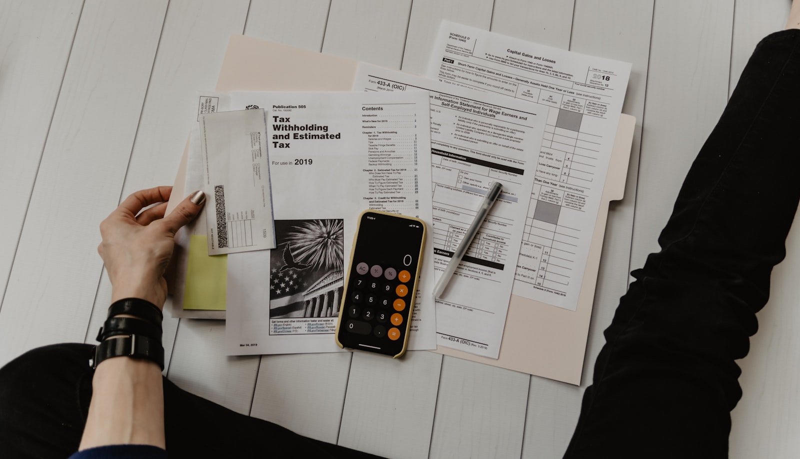 Mão a anotar números num caderno ao lado de uma calculadora e folhas com cálculos, em preparação de orçamento.